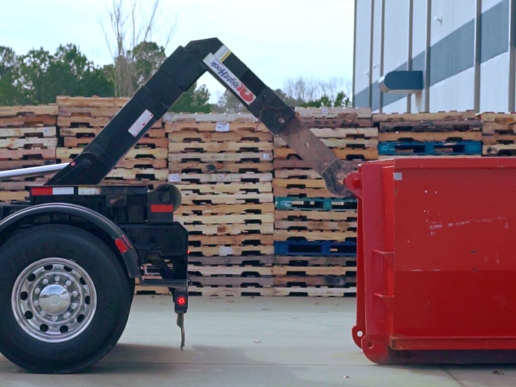 A Waste Removal USA truck arm preparing to hook or unhook a red roll-off dumpster for junk removal in Austin, TX