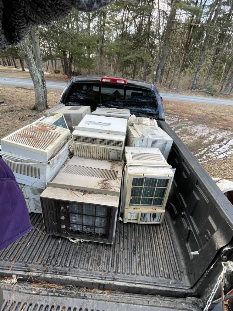 The bed of a pickup truck filled with numerous old window air conditioning units, collected by Nu Earth Hauling and Recycling in Allentown, PA.