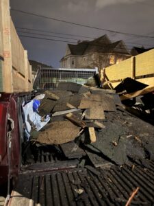 A Just Junk It truck bed filled with roofing debris and construction waste at night in Lancaster, PA.