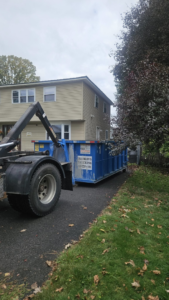 A Franklin's Disposal & Roll-Off Service truck delivering a blue dumpster to a residential driveway in Utica, NY.
