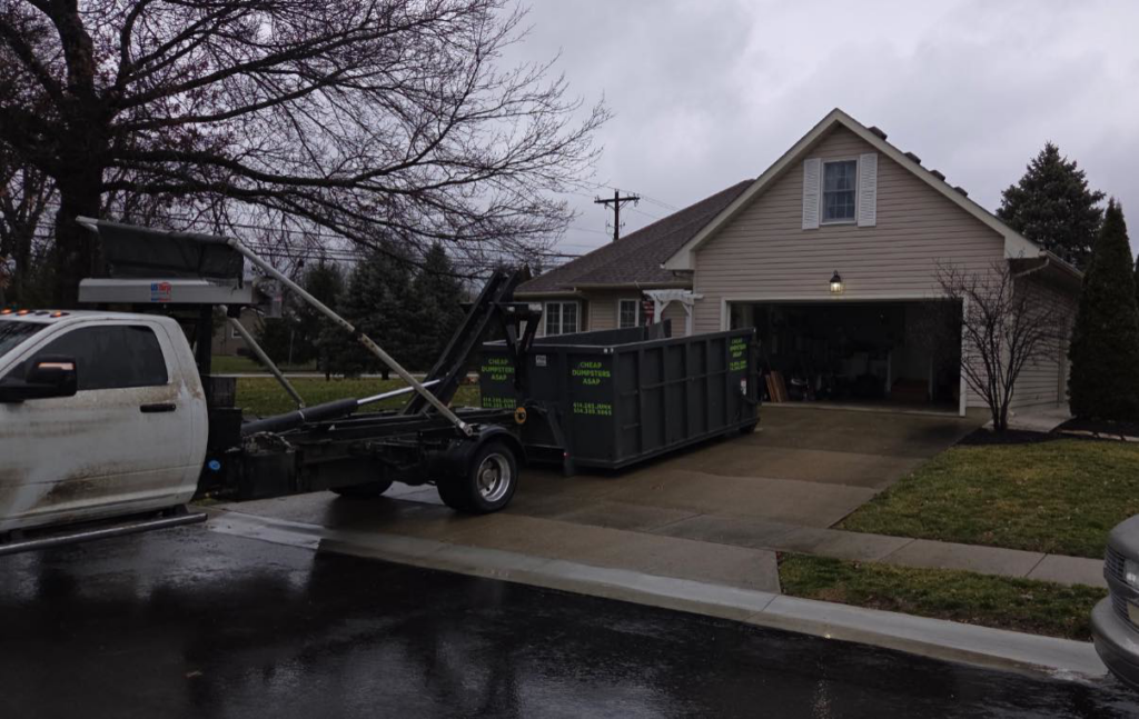 A truck delivering a dumpster to a residential driveway for junk removal by Cheap Dumpsters ASAP in Columbus, OH.