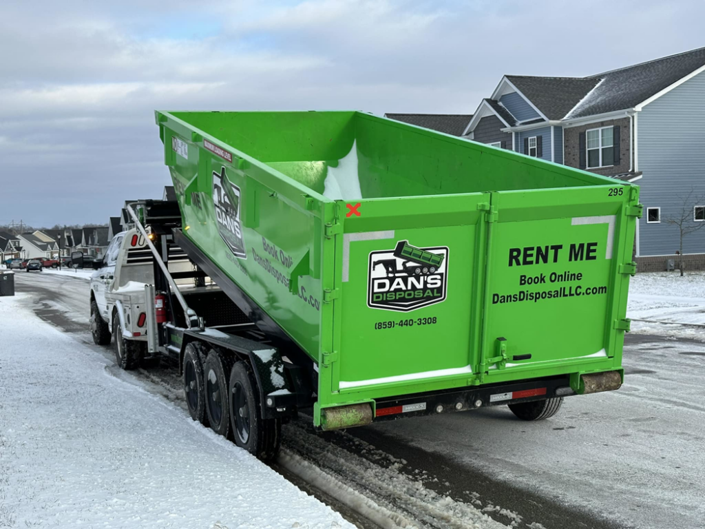 A Dan's Disposal LLC truck delivering a bright green dumpster on a snowy street in Richmond, KY.