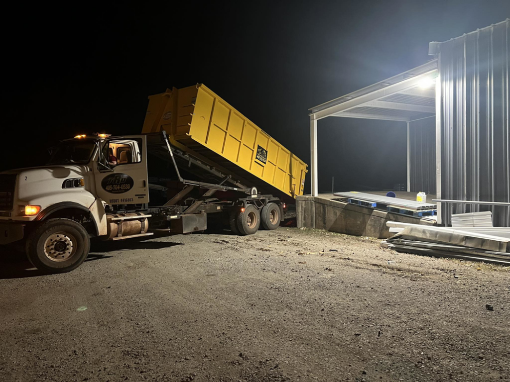 A large truck delivering a yellow roll-off dumpster at night for Tecumseh Rolloff Services in Moore, OK.
