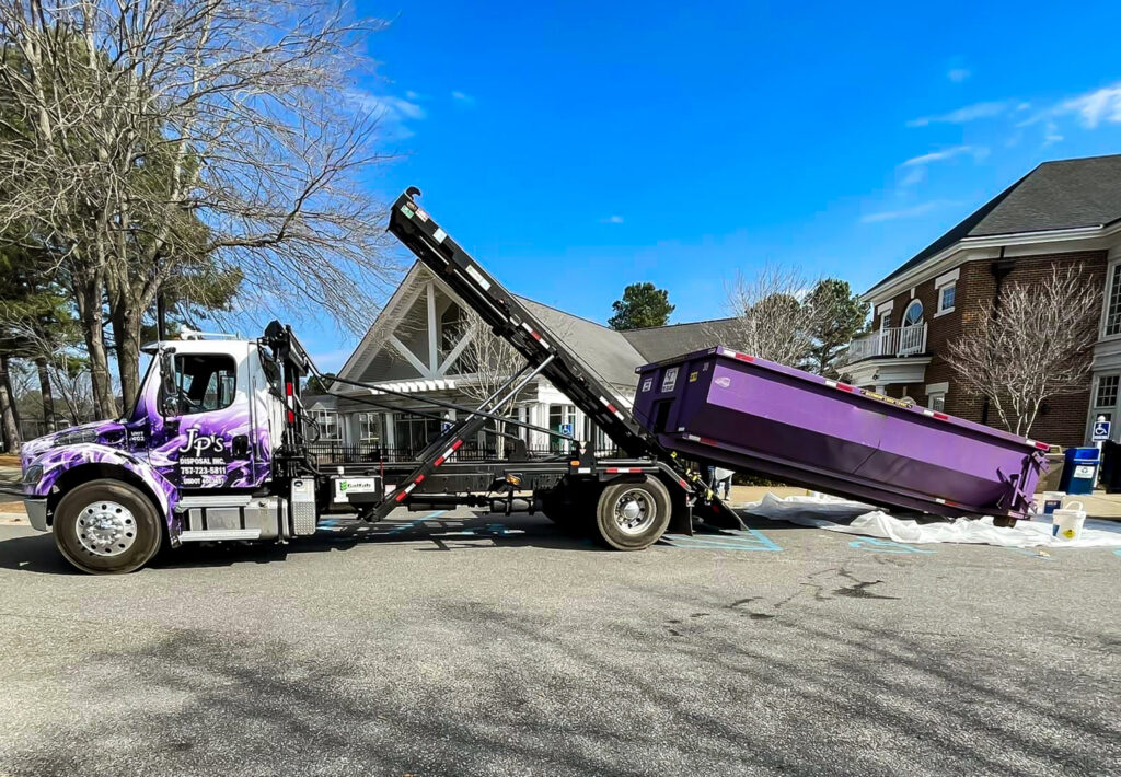 A JP's Disposal Inc. truck deploying a purple dumpster in a parking lot in Hampton, VA.