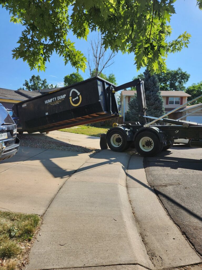 A Humpty Dump Roll-Offs & Dumpsters truck deploying a roll-off dumpster into a residential driveway in Commerce City, CO.