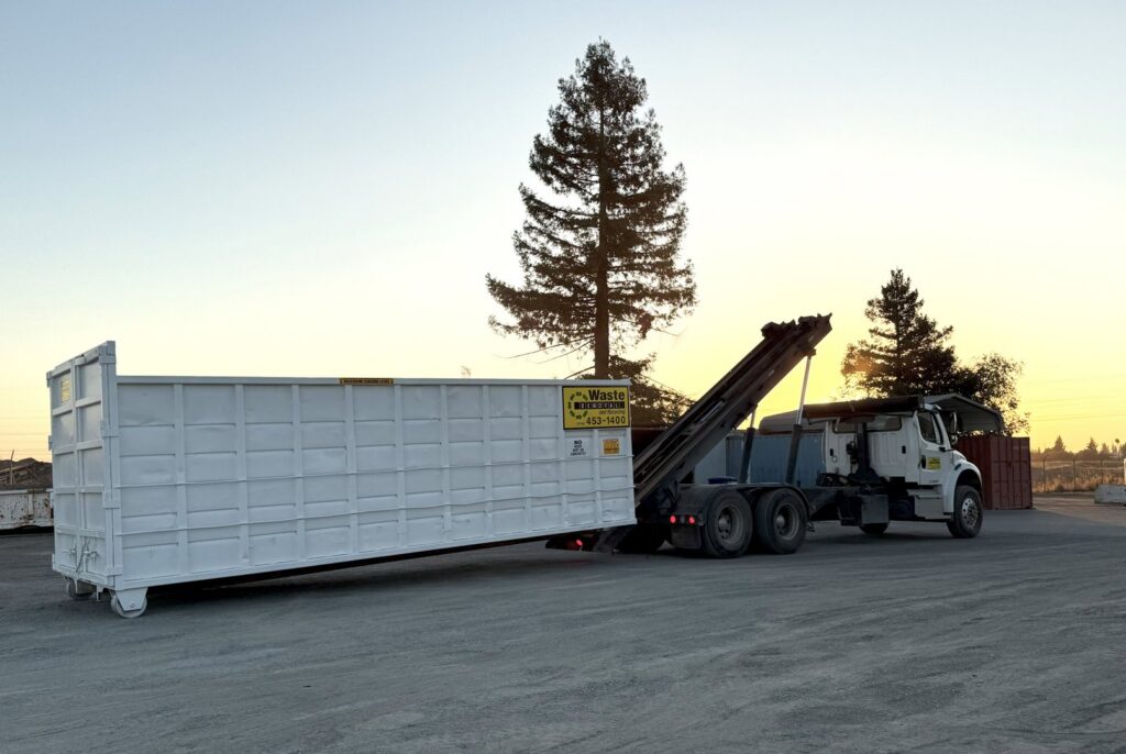 A Waste Removal and Recycling, Inc. truck deploying a roll-off dumpster at sunset in Sacramento, CA.
