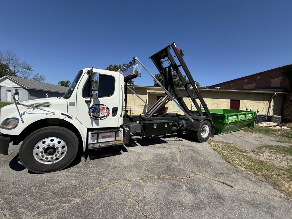 An American Dumpster Rentals truck deploying a green dumpster in a rural area in Morrilton, AR.