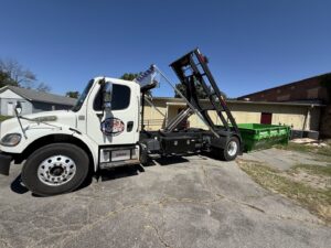 An American Dumpster Rentals truck deploying a green dumpster in a rural area in Morrilton, AR.