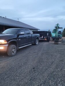 A black pickup truck with a dump trailer and an excavator, showing equipment used by Primetime Hauling and Junk Removal in Spokane, WA.