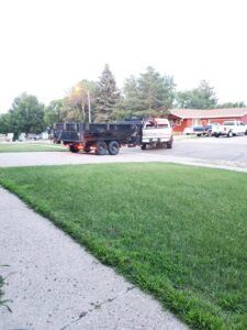 A white truck pulling a dump trailer on a residential street, ready for a junk removal job by Outlaw Rental in Bismarck, ND.