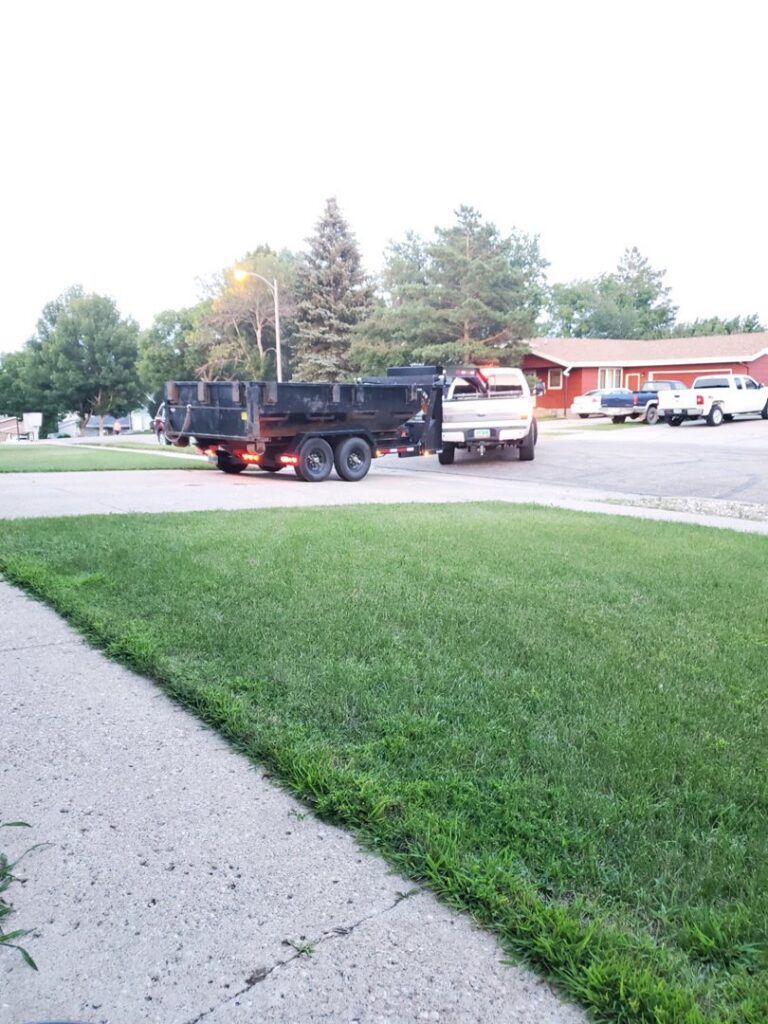 A white truck pulling a dump trailer on a residential street, ready for a junk removal job by Outlaw Rental in Bismarck, ND.