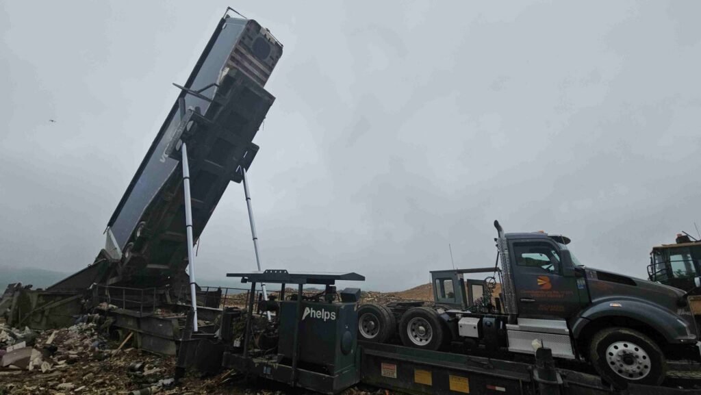 A Voyager Trucking semi-truck with a raised trailer dumping debris at a landfill or transfer station in Newark, NJ