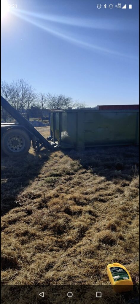 A FJD Waste Disposal and Recycling LLC truck with a green dumpster positioned in a grassy field for waste collection in Dallas, TX.