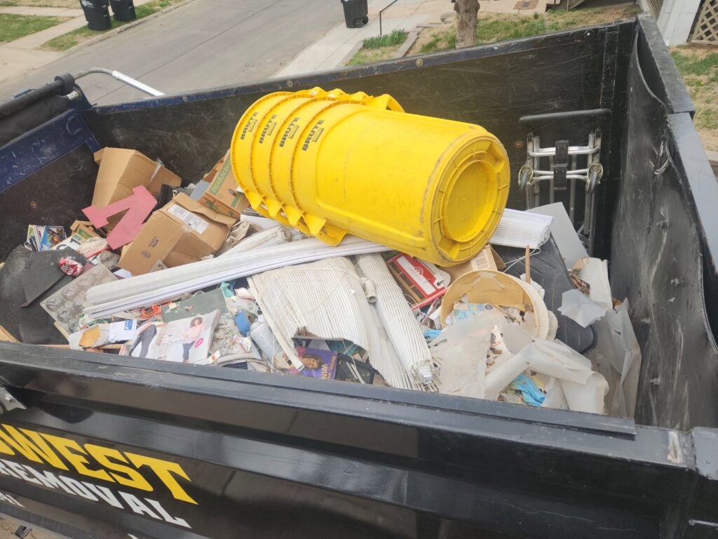 A Midwest Removal truck filled with various junk items, including yellow bins and cardboard, in Omaha, NE.