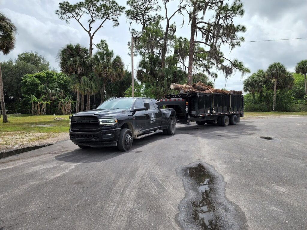 A Silverback Dumpster Rentals truck hauling a dump trailer filled with logs and tree branches in LaBelle, FL.