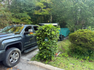 A pickup truck hauling a blue dumpster on a trailer for Site Boss Dumpster Rentals in Raeford, NC.