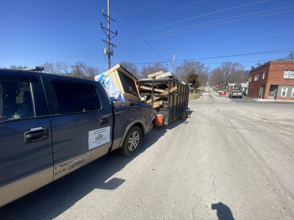A Harris Family Hauling & Snow Removal LLC truck pulling a trailer loaded with junk on a street in Independence, MO.