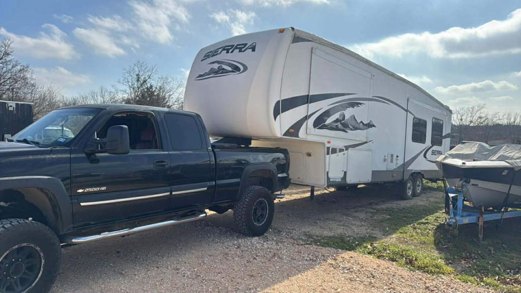 A black pickup truck hauling a white Sierra fifth-wheel RV for Trash Junkies & Transport Services in Thornville, OH.