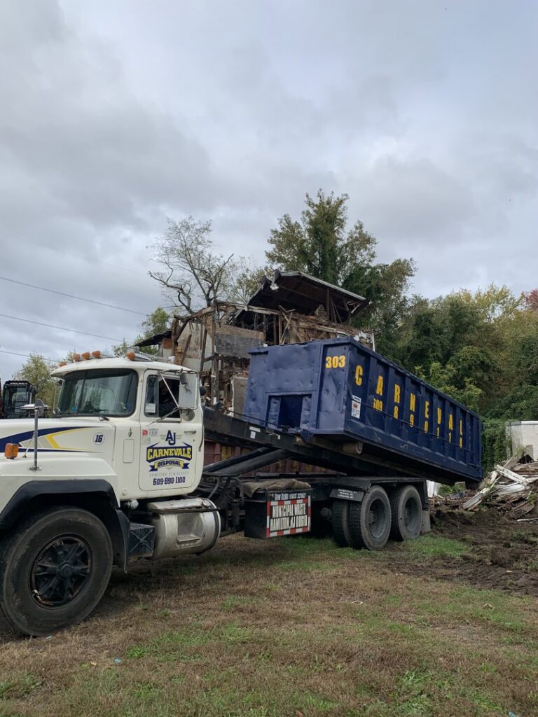 An AJ Carnevale Disposal truck lifting a dumpster at a demolition site in Hamilton, NJ