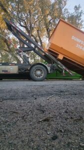 A J & A Haul Away & Dumpster Rentals truck lifting an orange dumpster, demonstrating service in Derby, KS.