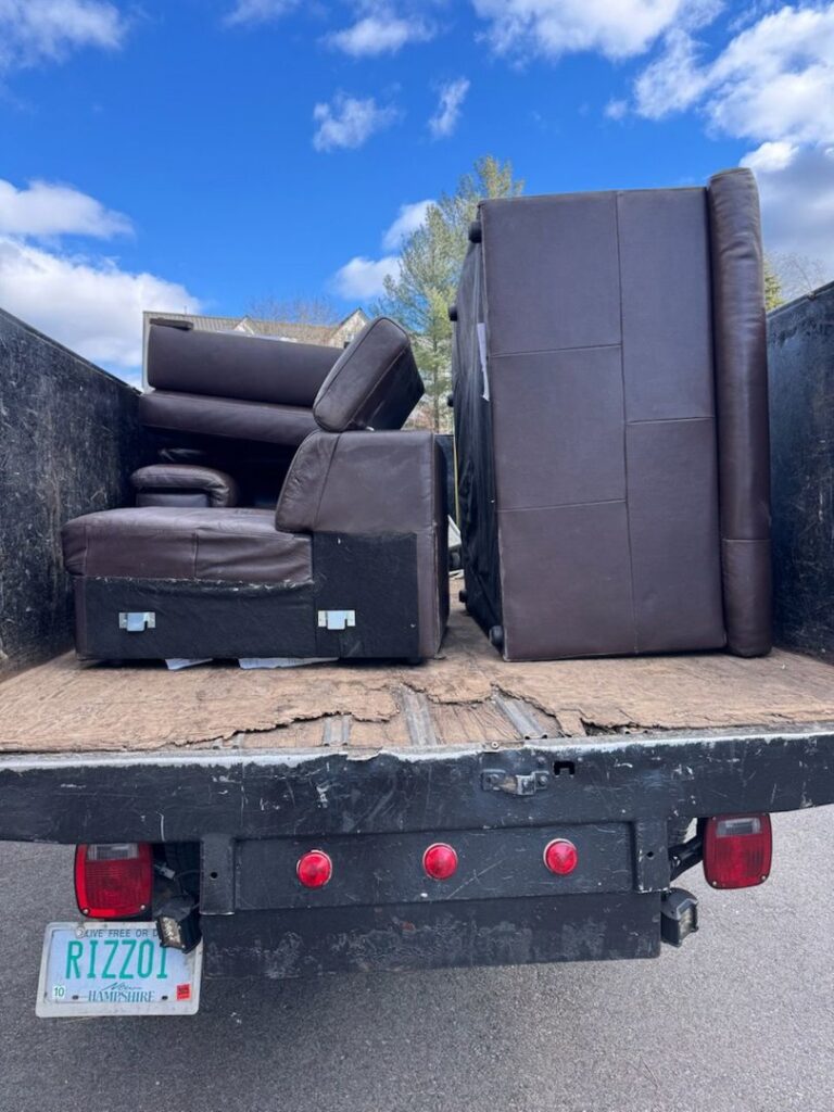 The back of a Rizzo Junk Removal truck loaded with large brown couches and furniture in Nashua, NH.