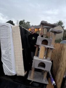 A worker from Tiny Monster Junk Removal LLC in Denver, CO, standing next to a truck loaded with mattresses and a cat tree.