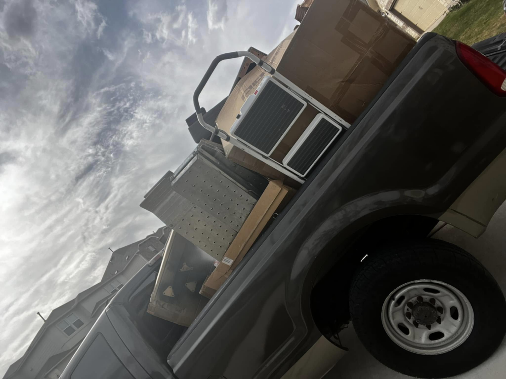 A pickup truck loaded with mixed junk, including an old AC unit and cardboard boxes, by ONLY Junk Removal Services in Austin, TX.