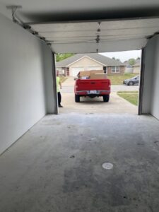 A red pickup truck loaded with cardboard boxes, seen from inside a garage, indicating a cleanout or hauling service by Little Tykes Property Preservation in Independence, MO.