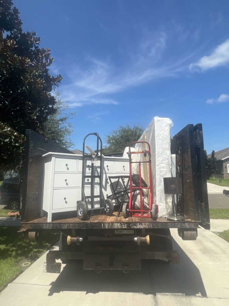 The back of a junk removal truck loaded with a dresser, mattress, and dollies for Lightning Bay Junk Removal in Tampa, FL.