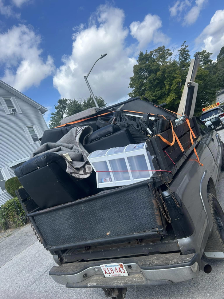 A junk removal truck loaded with old furniture and various household items, secured for transport by Trash Hogs in Worcester, MA.