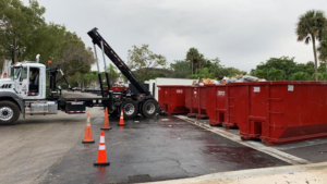 A hook-lift truck with multiple red dumpsters, some filled with junk, for Dumpster Rental Florida in West Park, FL.