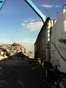 A Voyager Trucking semi-truck parked next to a large outdoor pile of junk and waste in Newark, NJ