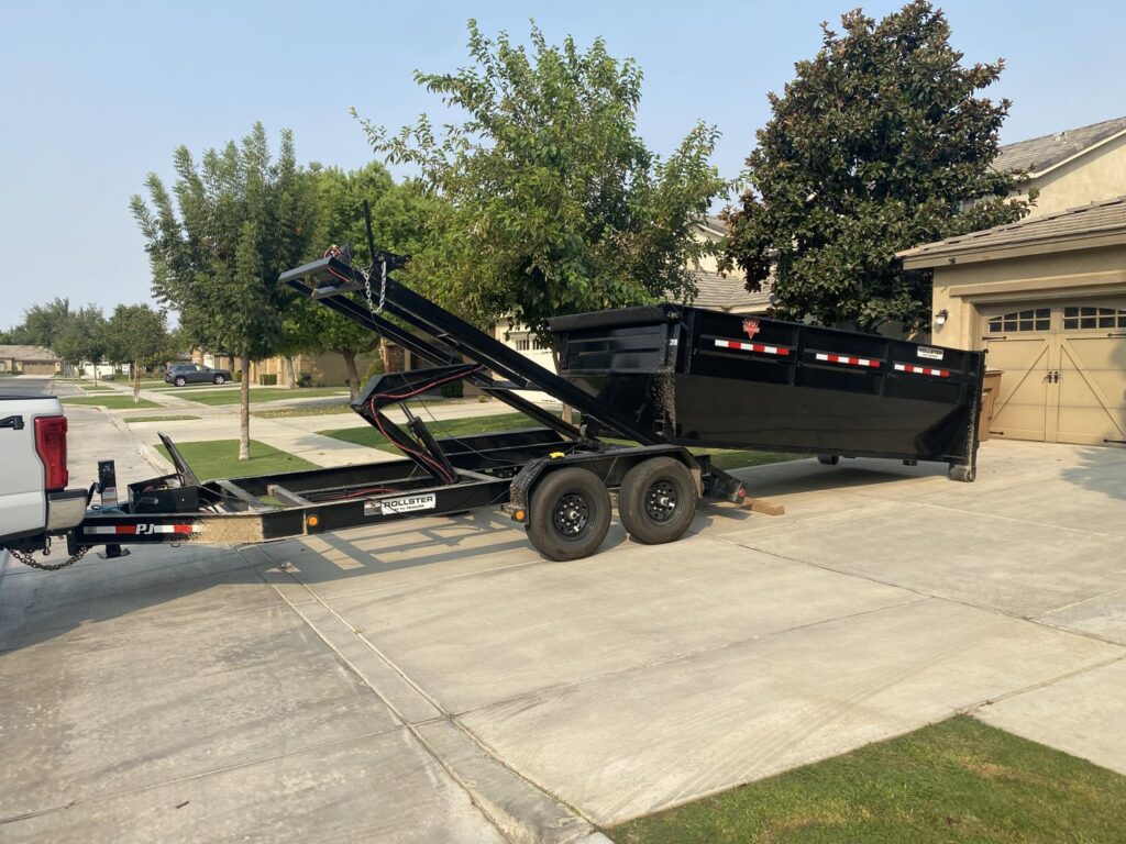 A truck with a roll-off trailer and an empty dumpster in a residential driveway from Bakersfield Roll-Off Service in Bakersfield, CA.