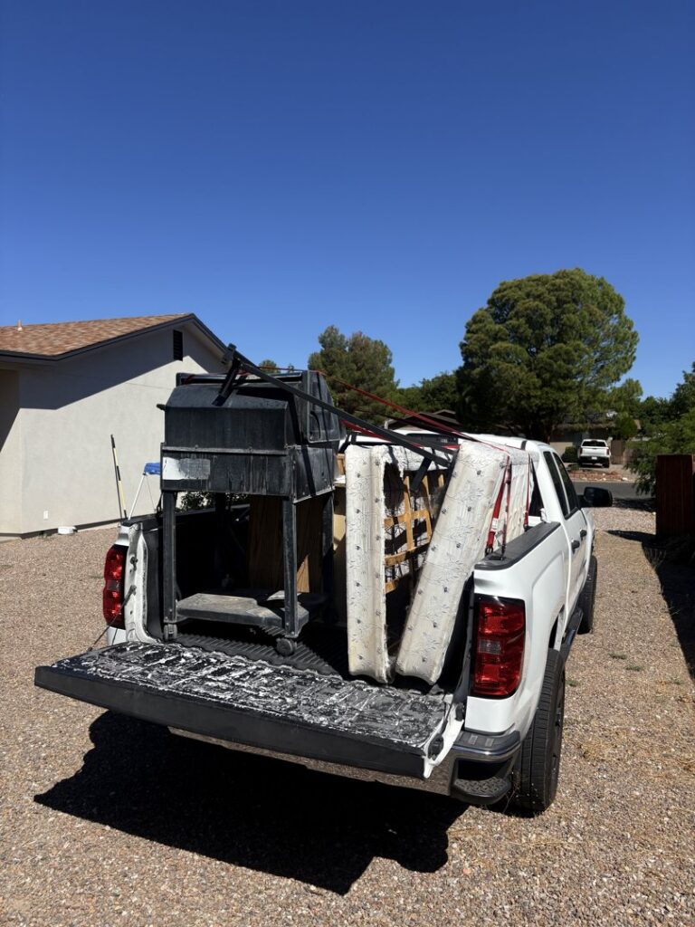 A richartehelps pickup truck with its tailgate down, loaded with a grill, cushions, and other junk for removal in Scottsdale, AZ.