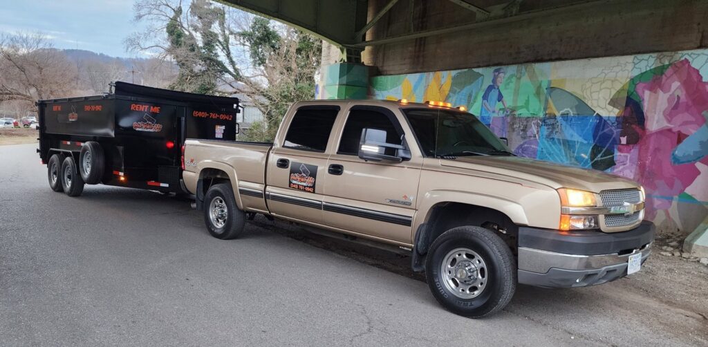 A Haul Rollers LLC pickup truck towing a dump trailer under a bridge, transporting junk in Roanoke, VA.