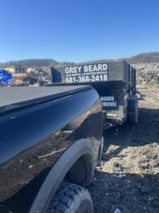 A Greybeard Dumpster Rentals truck towing a dumpster trailer at a landfill for junk disposal in Morgantown, WV.