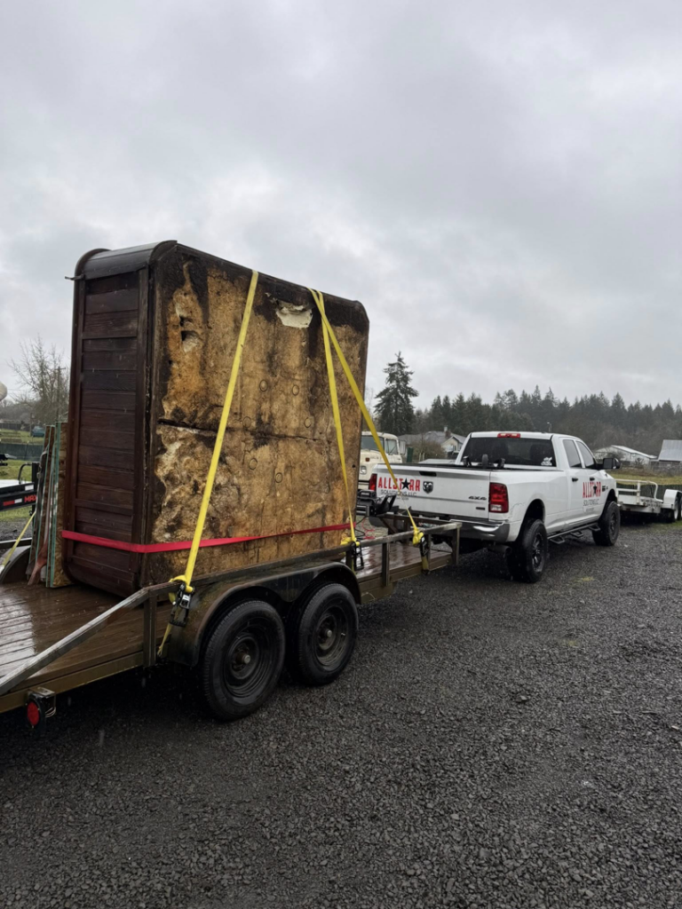 An AllStarr Solutions Hauling and Junk Removal truck towing a large hot tub on a trailer in Newberg, OR.