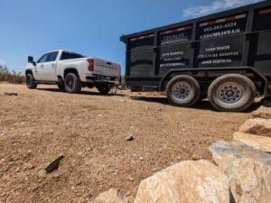 A white truck towing a black CzechList Junk Removal trailer through a desert landscape in Scottsdale, AZ.