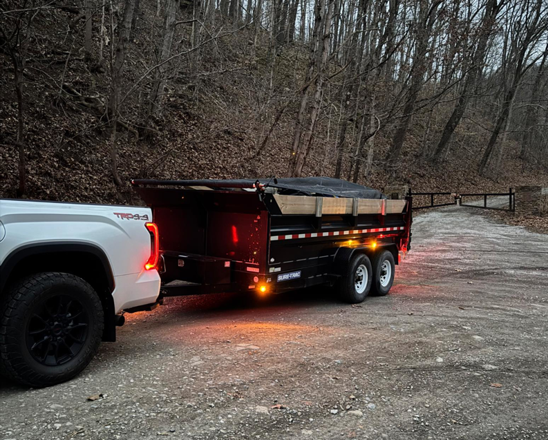 A white pickup truck towing a loaded dump trailer with covered debris for Trash & Dash in Houston, TX.