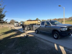 A pickup truck towing a dump trailer loaded with junk and debris down a road for Tidy Loaders Junk Removal in Houston, TX.