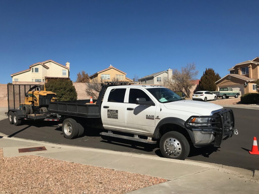 A Kiki's Tree Service truck towing a stump grinder on a trailer, ready for a job in Albuquerque, NM.