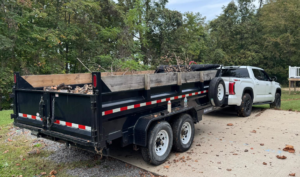 A pickup truck towing a dump trailer filled with yard waste and branches for Trash & Dash in Houston, TX.