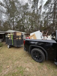 A black pickup truck towing a trailer filled with furniture and various items for junk removal by Reliable Pro in Tallahassee, FL.