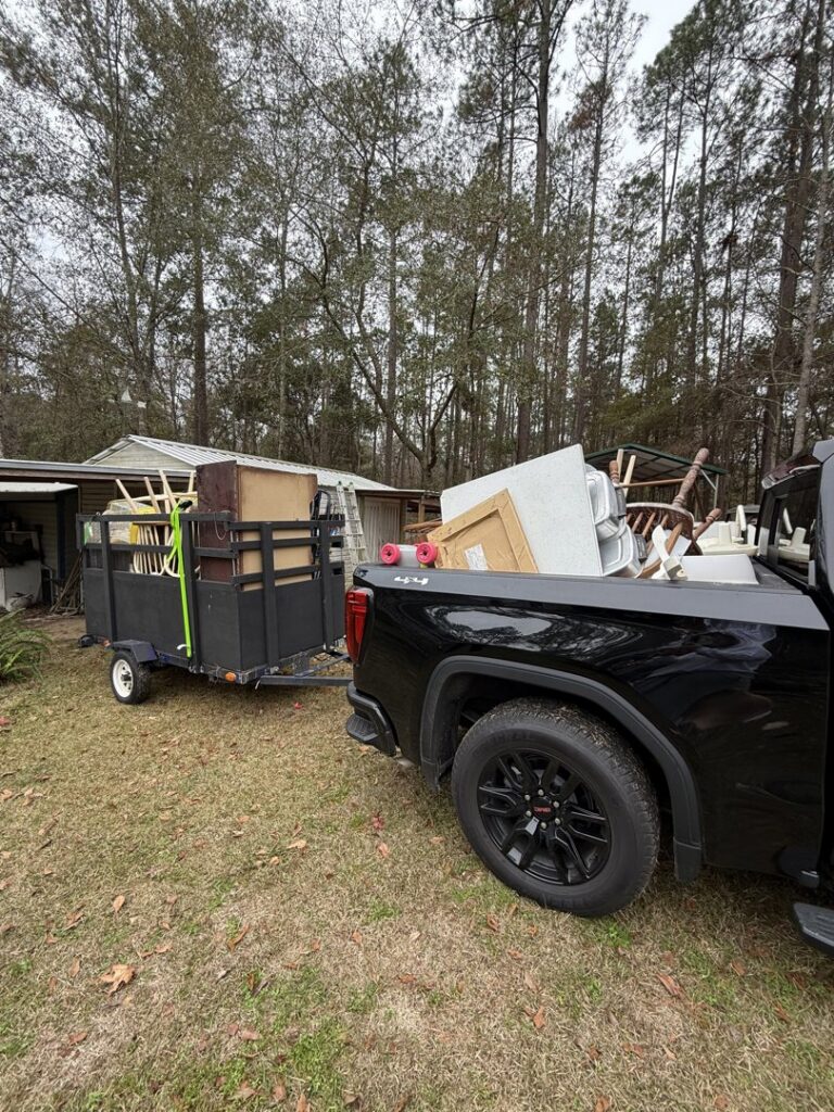 A black pickup truck towing a trailer filled with furniture and various items for junk removal by Reliable Pro in Tallahassee, FL.