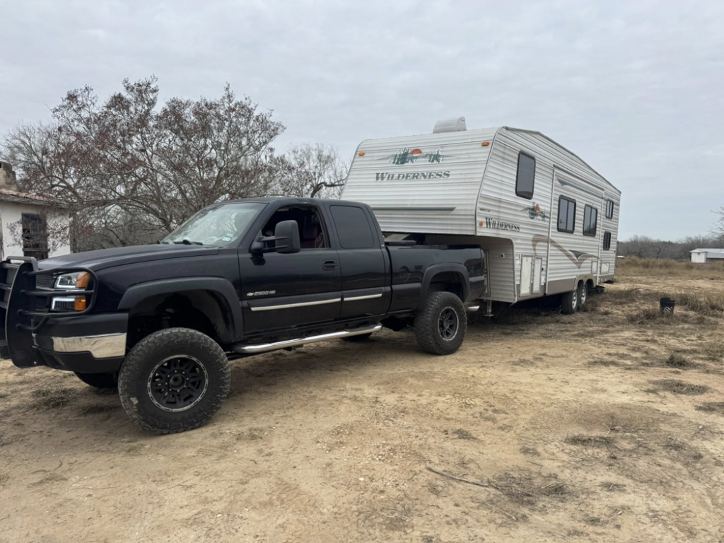 A black pickup truck towing a white Wilderness fifth-wheel RV for Trash Junkies & Transport Services in Thornville, OH.