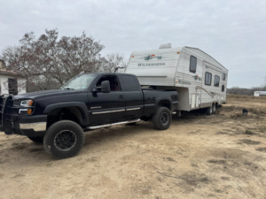A black pickup truck towing a white Wilderness fifth-wheel RV for Trash Junkies & Transport Services in Thornville, OH.