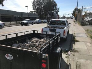 A truck pulling a trailer loaded with construction debris and rocks, handled by Dan's Home and Yard in Oakland, CA.