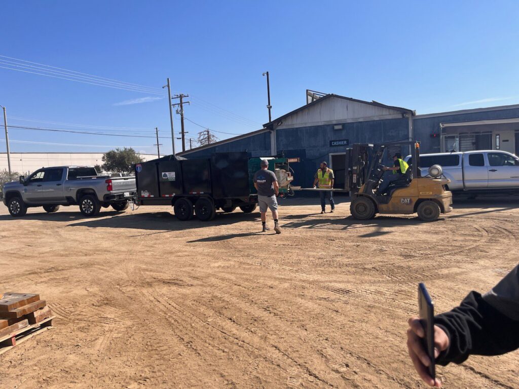 A Valley Haul Off LLC truck and dump trailer at a commercial site, with a forklift assisting in a hauling operation in Visalia, CA.