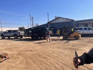 A Valley Haul Off LLC truck and dump trailer at a commercial site, with a forklift assisting in a hauling operation in Visalia, CA.