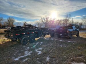 A pickup truck pulling a dump trailer full of various junk items, demonstrating a job by Rubble Removers LLC in Riverton, WY.